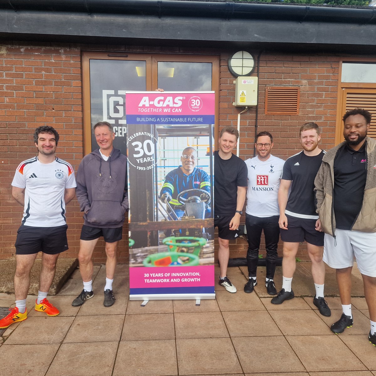 A group of men in sportswear stand around an upright A-Gas banner