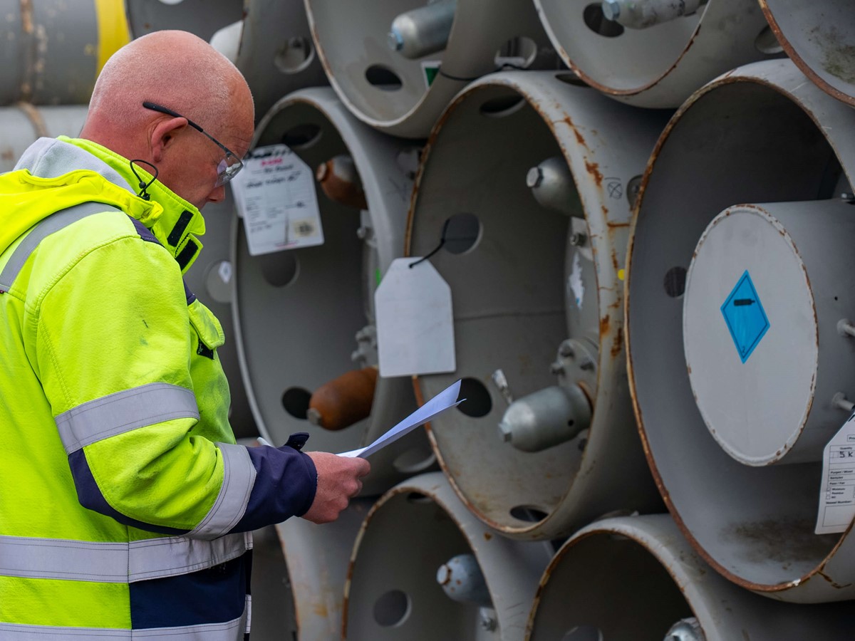 Man in a yellow hi-vis jacket reading in front of silver cylinders