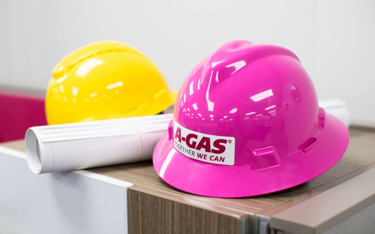 A close-up image of a pink hardhat with the A-Gas logo on the front in an office