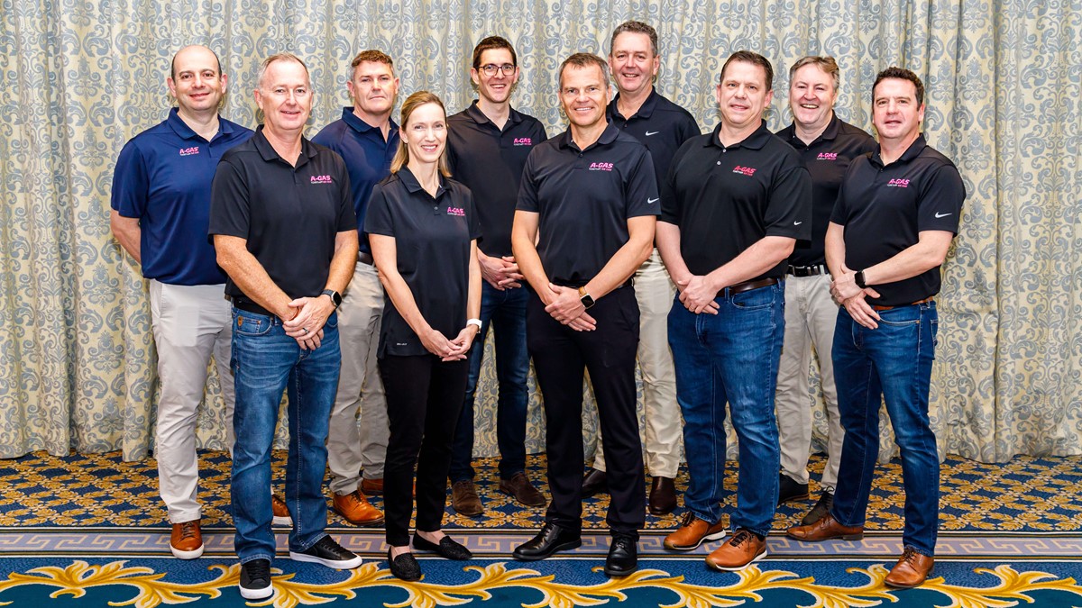 A group of people smile at the camera with a patterned curtain in the background