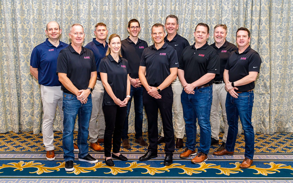 A group of people smile at the camera with a patterned curtain in the background