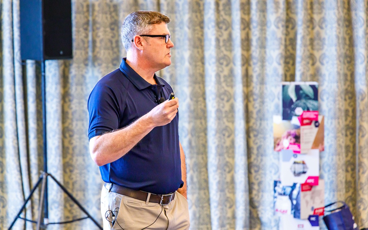 A man wearing glasses and a blue polo shirt delivering a presentation side-on